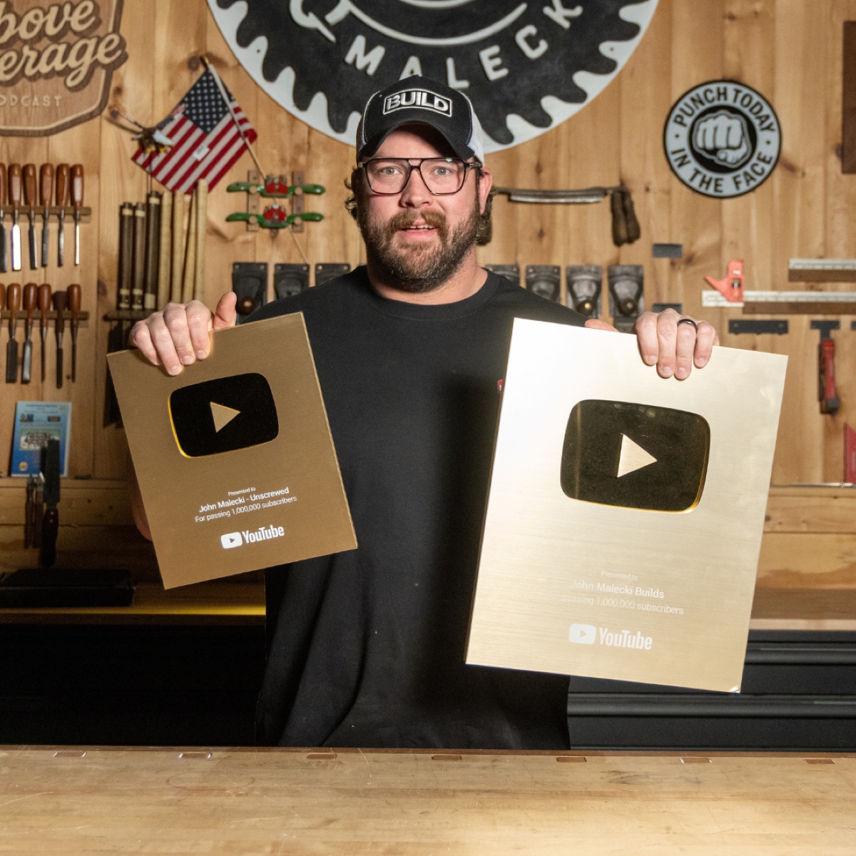 John Malecki in his shop holding two gold YouTube play button awards