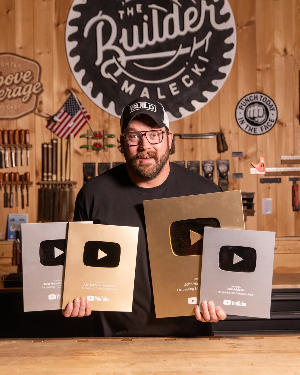 John Malecki in his shop holding four YouTube play button awards